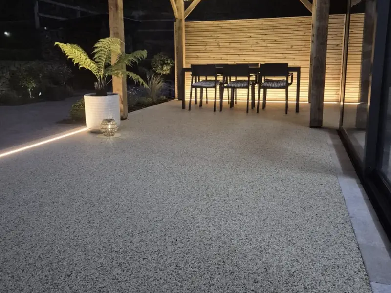 Resin bound patio under a lit timber pergola at dusk