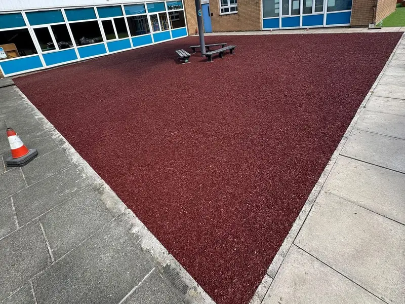 Red rubber play surface installed by T&A Resin in a school courtyard under a shade sail